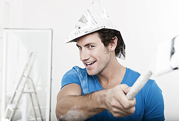 Germany, Cologne, Close up of young man wearing paper hat painting in renovating apartment - FMKF000328