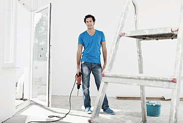 Germany, Cologne, Young man holding electric drill in renovating apartment - FMKF000329