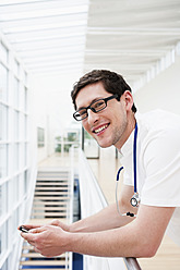 Germany, Bavaria, Diessen am Ammersee, Young doctor leaning and holding mobile phone, smiling - JRF000188