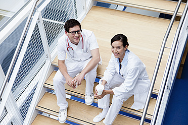 Deutschland, Bayern, Diessen am Ammersee, Zwei junge Ärzte mit Einwegbechern auf einer Treppe sitzend, lächelnd, Porträt - JRF000202