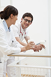 Germany, Bavaria, Diessen am Ammersee, Two young doctors leaning and holding disposable cups, smiling - JRF000203