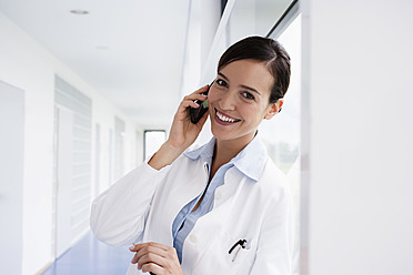 Deutschland, Bayern, Diessen am Ammersee, Junge Ärztin spricht mit Handy und lehnt sich an, lächelnd - JRF000247