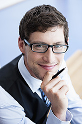 Deutschland, Bayern, Diessen am Ammersee, Nahaufnahme eines Geschäftsmannes mit dicker Brille, der einen Stift hält, lächelnd, Porträt - JRF000316