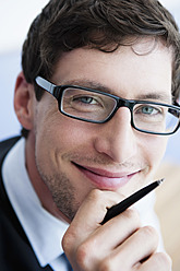 Deutschland, Bayern, Diessen am Ammersee, Nahaufnahme eines Geschäftsmannes mit dicker Brille, der einen Stift hält, lächelnd, Porträt - JRF000318