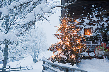 Österreich, Salzburger Land, Flachau, Blick auf beleuchteten Weihnachtsbaum mit Schlitten vor einer Almhütte - HHF003764