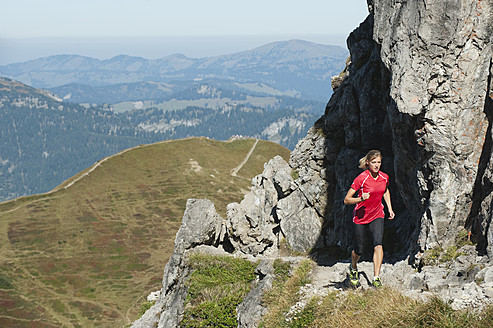 Austria, Kleinwalsertal, Young woman running on mountain trail near rocks - MIRF000274