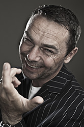 Close up of mature man making funny faces against black background, smiling, portrait - MAEF003545