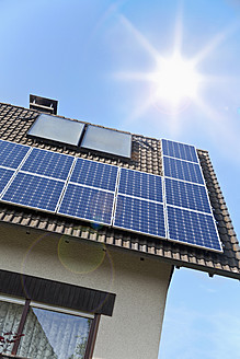 Germany, Cologne, Solar panels on rooftop against blue sky and sun - TSF000329