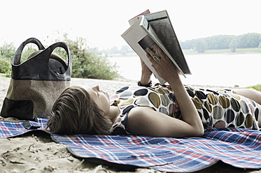 Germany, Rheinland, Young woman lying on blanket and reading book - LFOF000125