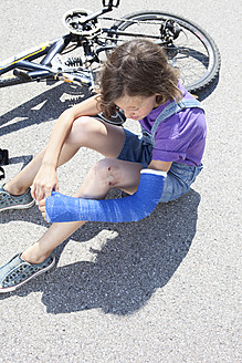 Deutschland, Bayern, Verletztes Mädchen sitzt nach Fahrradunfall auf der Straße - MAEF003572