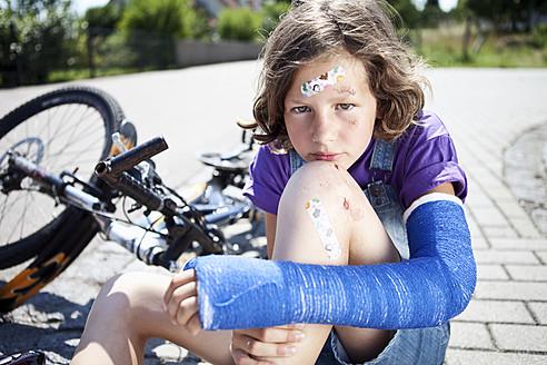 Deutschland, Bayern, Verletztes Mädchen sitzt nach Fahrradunfall auf der Straße - MAEF003575