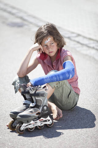Deutschland, Bayern, Verletztes Mädchen sitzt nach Inline-Skating-Unfall auf der Straße, lizenzfreies Stockfoto