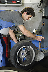 Germany, Ebenhausen, Mechatronic technician working on tyre in car garage - TCF001618