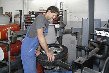 Germany, Ebenhausen, Mechatronic technician working on tyre in car garage - TCF001619