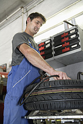 Germany, Ebenhausen, Mechatronic technician working on tyre in car garage - TCF001620