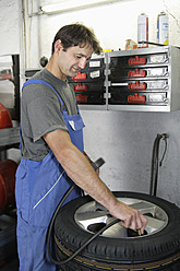 Germany, Ebenhausen, Mechatronic technician working on tyre in car garage - TCF001621