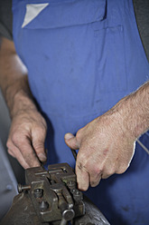 Germany, Ebenhausen, Mechatronic technician working on machine part in car garage, close up - TCF001634