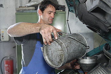 Germany, Ebenhausen, Mechatronic technician pouring oil in car at car garage - TCF001643