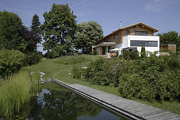 Deutschland, Oberbayern, München, Blick auf einen Teich vor einem neuen Holzhaus im Dorf - TCF001672