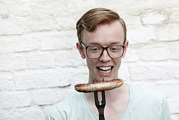 Germany, Berlin, Close up of young man with grilled sausage, smiling - WESTF016914