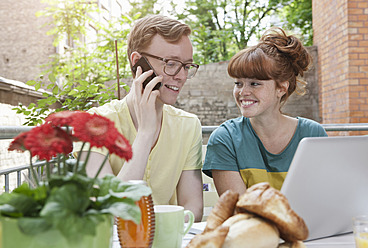 Germany, Berlin, Young couple using cell phone and laptop, smiling - WESTF016940