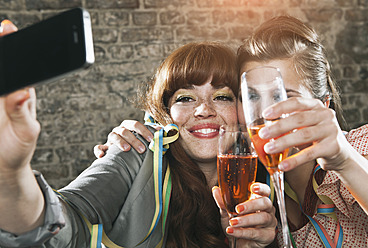 Germany, Berlin, Close up of young women holding champagne glass and photographing with cell phone, smiling - WESTF016946