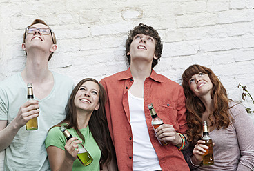 Deutschland, Berlin, Junge Männer und Frauen, die Bierflaschen halten und lächelnd nach oben schauen - WESTF016977