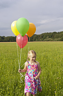 Deutschland, Nordrhein-Westfalen, Hennef, Mädchen hält Luftballons und läuft durch eine Wiese - KJF000127