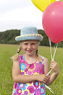 Deutschland, Nordrhein-Westfalen, Hennef, Mädchen hält Luftballons und steht auf einer Wiese - KJF000130