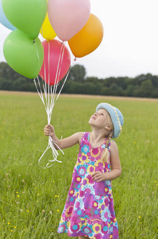 Deutschland, Nordrhein-Westfalen, Hennef, Mädchen hält Luftballons und steht auf einer Wiese, lizenzfreies Stockfoto