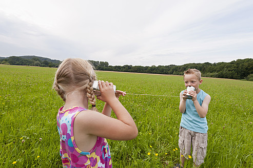 Germany, North Rhine-Westphalia, Hennef, Boy and girl in meadow playing with tin can phone - KJF000134