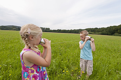 Germany, North Rhine-Westphalia, Hennef, Boy and girl in meadow playing with tin can phone - KJF000135