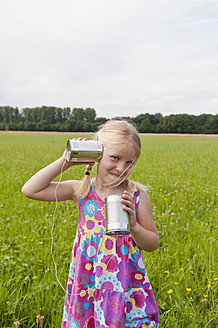 Germany, North Rhine-Westphalia, Hennef, Girl standing in meadow and playing with tin can phone - KJF000136