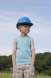 Deutschland, Nordrhein-Westfalen, Hennef, Junge mit Bauarbeiterhelm steht auf einer Wiese - KJF000139