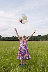 Germany, North Rhine-Westphalia, Hennef, Girl throwing beach ball globe in meadow - KJF000147