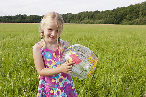 Germany, North Rhine-Westphalia, Hennef, Girl standing with beach ball globe in meadow - KJF000143