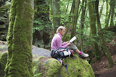 Germany, Rhineland-Palatinate, Eifel Region, South Eifel Nature Park, View of woman hiker sitting on bunter rock formations at beech tree forest - GWF001533