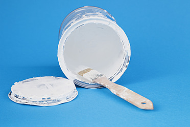 Used paint brush in white varnish of paint tin on blue background, close up - GWF001572