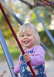 Germany, Munich, Girl climbing on climbing frame in playground, smiling, portrait - HSIF000126