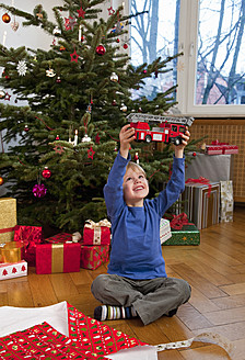 Germany, Munich, Boy sitting christmas present holding toy fire engine - HSIF000142