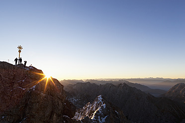 Germany, Bavaria, Bavarian Alps, Wetterstein Range, View of cross on summit of Zugspitze with hikers at sunrise - FO003585