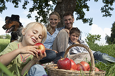Deutschland, Bayern, Altenthann,Mädchen mit Korb voller Äpfel, Familie mit Hund im Hintergrund - RBF000699