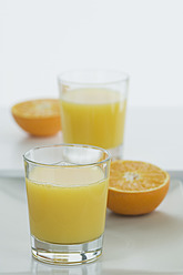 Gläser mit Orangensaft und halben Orangen auf dem Tisch - ASF004411