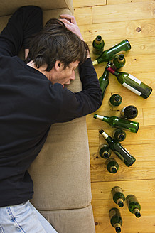 Germany, Hessen, Frankfurt, Drunk man lying on sofa with empty beer bottles - MUF001036
