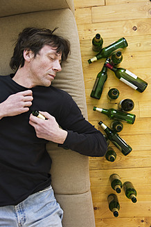 Deutschland, Hessen, Frankfurt, Betrunkener Mann auf Sofa liegend mit leeren Bierflaschen - MUF001037
