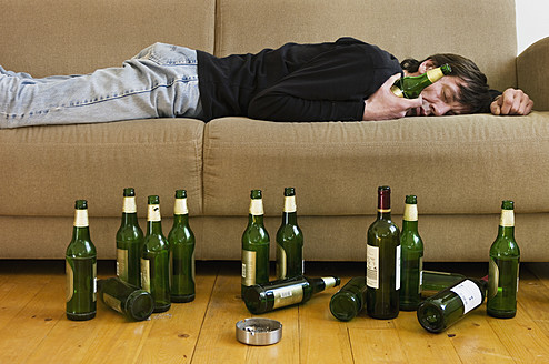 Germany, Hessen, Frankfurt, Drunk man lying on sofa with empty beer bottles - MUF001038