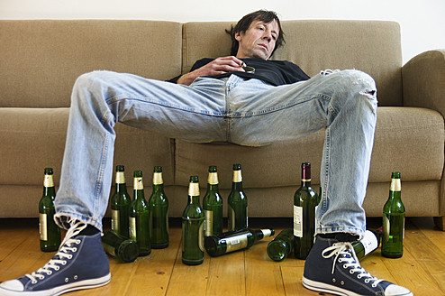Germany, Hessen, Frankfurt, Drunk man lying on sofa with empty beer bottles - MUF001040