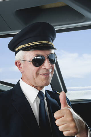 Germany, Bavaria, Munich, Senior flight captain wearing aviation glasses with thumbs up in airplane cockpit, smiling, close up stock photo