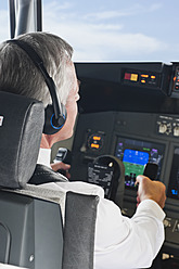 Deutschland, Bayern, München, Senior Flugkapitän trägt Kopfhörer und steuert aus dem Cockpit eines Flugzeugs - WESTF017025