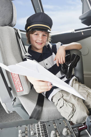 Deutschland, Bayern, München, Junge mit Kapitänsmütze und Papierflugzeug im Cockpit eines Flugzeugs, lizenzfreies Stockfoto